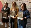 Three people holding awards plaques