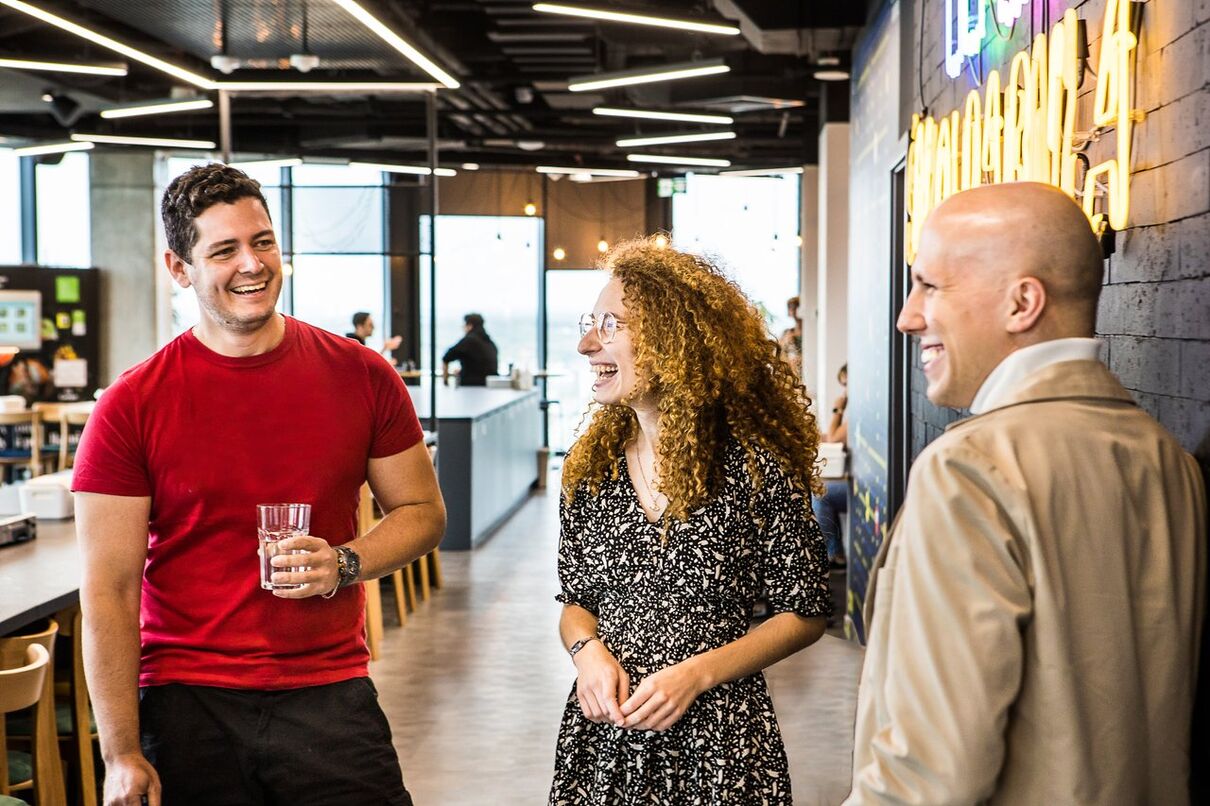 Three colleagues chatting and laughing together in a modern office space.
