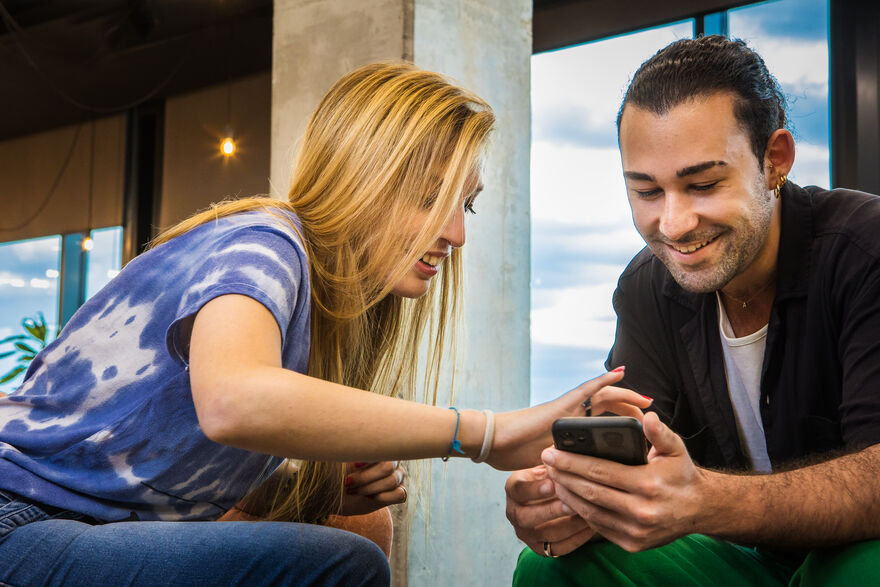 Un homme regarde son téléphone tandis qu’une femme passe son doigt sur l’écran; les deux sourient. 