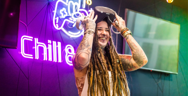Woman smiling, while taking off VR headset. A neon sign behind her on the wall.