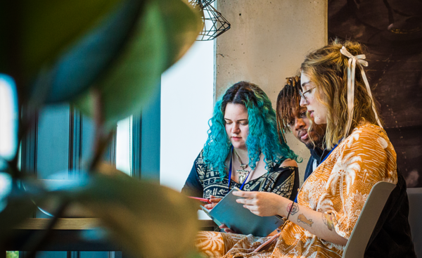 Three colleagues sitting together by a window, collaborating and reviewing notes on a tablet.